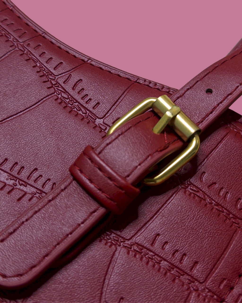 Close-up of a red leather belt with a gold buckle on a pink background