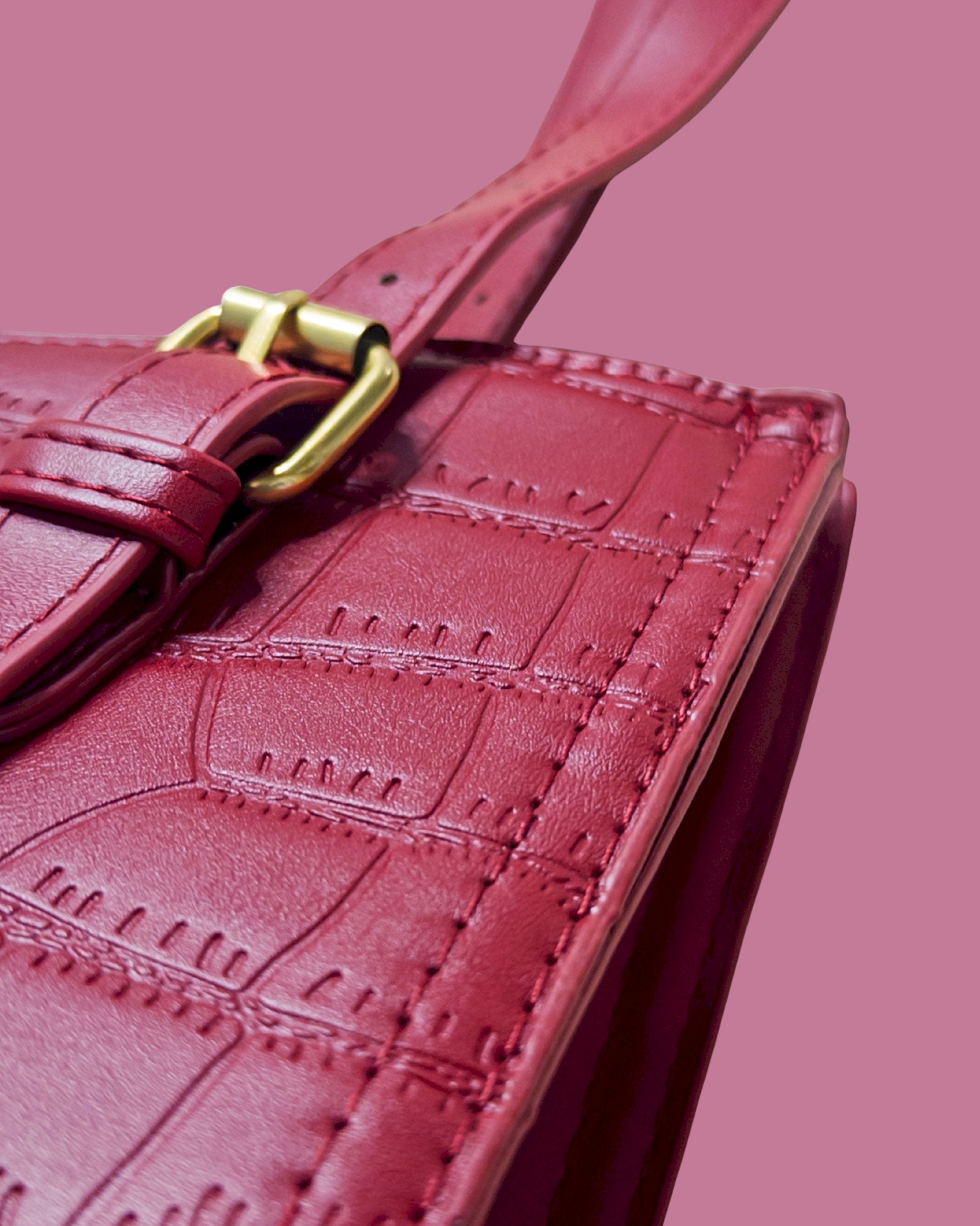 Close-up of a red leather handbag with a gold buckle on a pink background