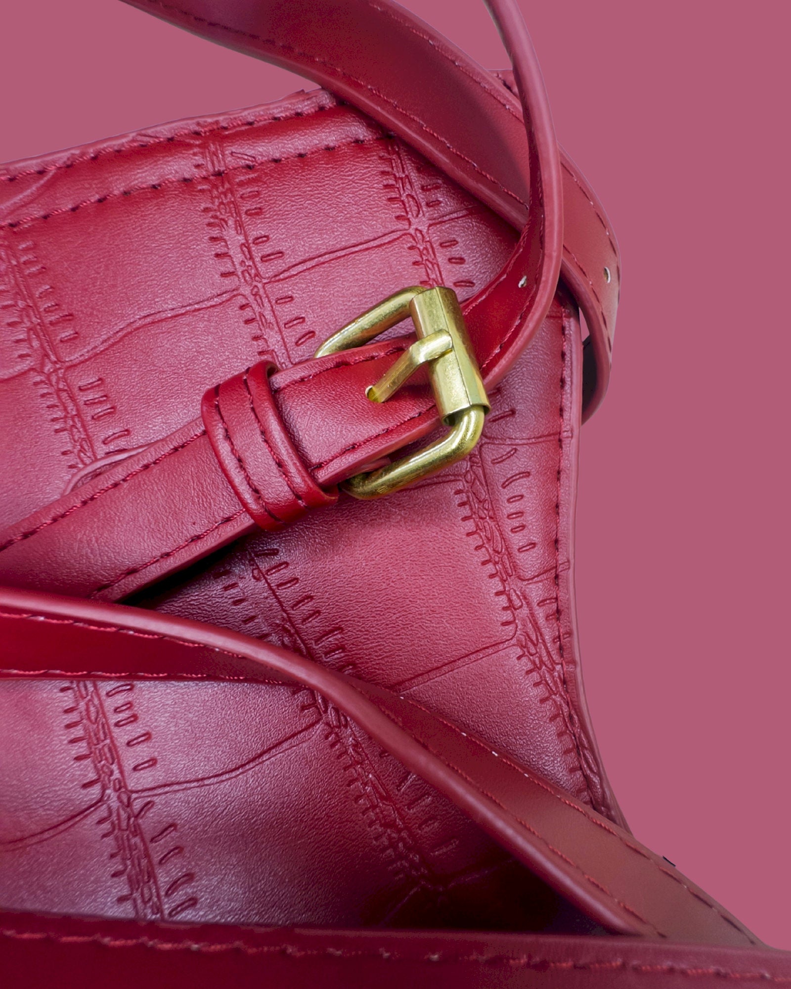 Close-up of a red textured handbag with a gold buckle on a pink background
