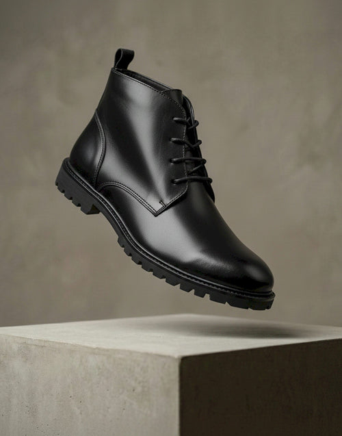 Black leather boot on a concrete block with a neutral background