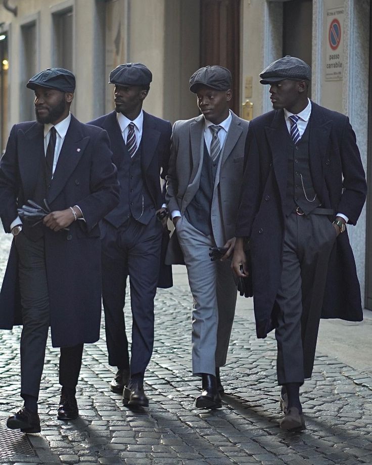 Four men in suits and hats walking together on a cobblestone street.